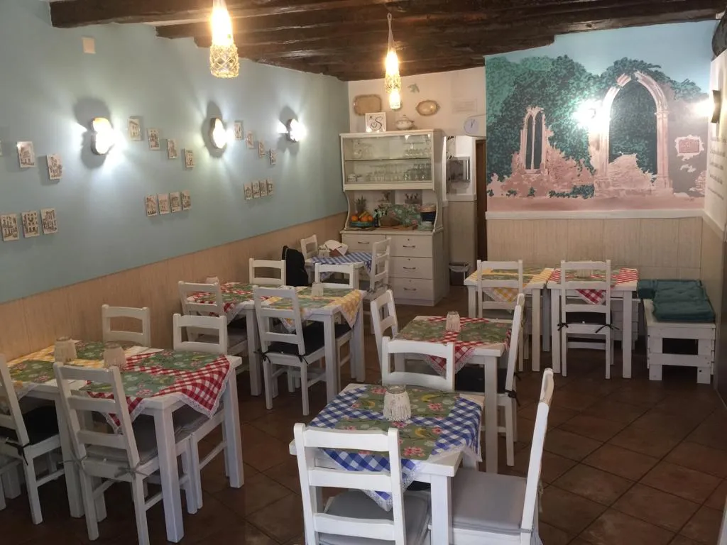 A sala da Tasquinha: paredes verde-água, mesas brancas com toalhas de quadrados e o mural das ruínas ao fundo
